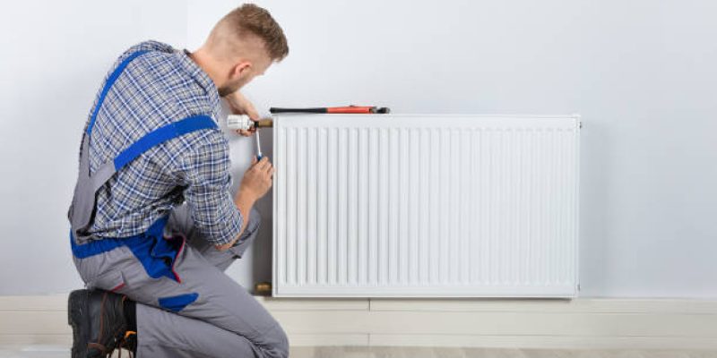 Rear View Of Male Plumber Fixing Thermostat With Screwdriver And Wrench On Radiator
